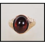 A hallmarked 15ct gold ring set with a red garnet cabochon, having engraved shank and shoulders.