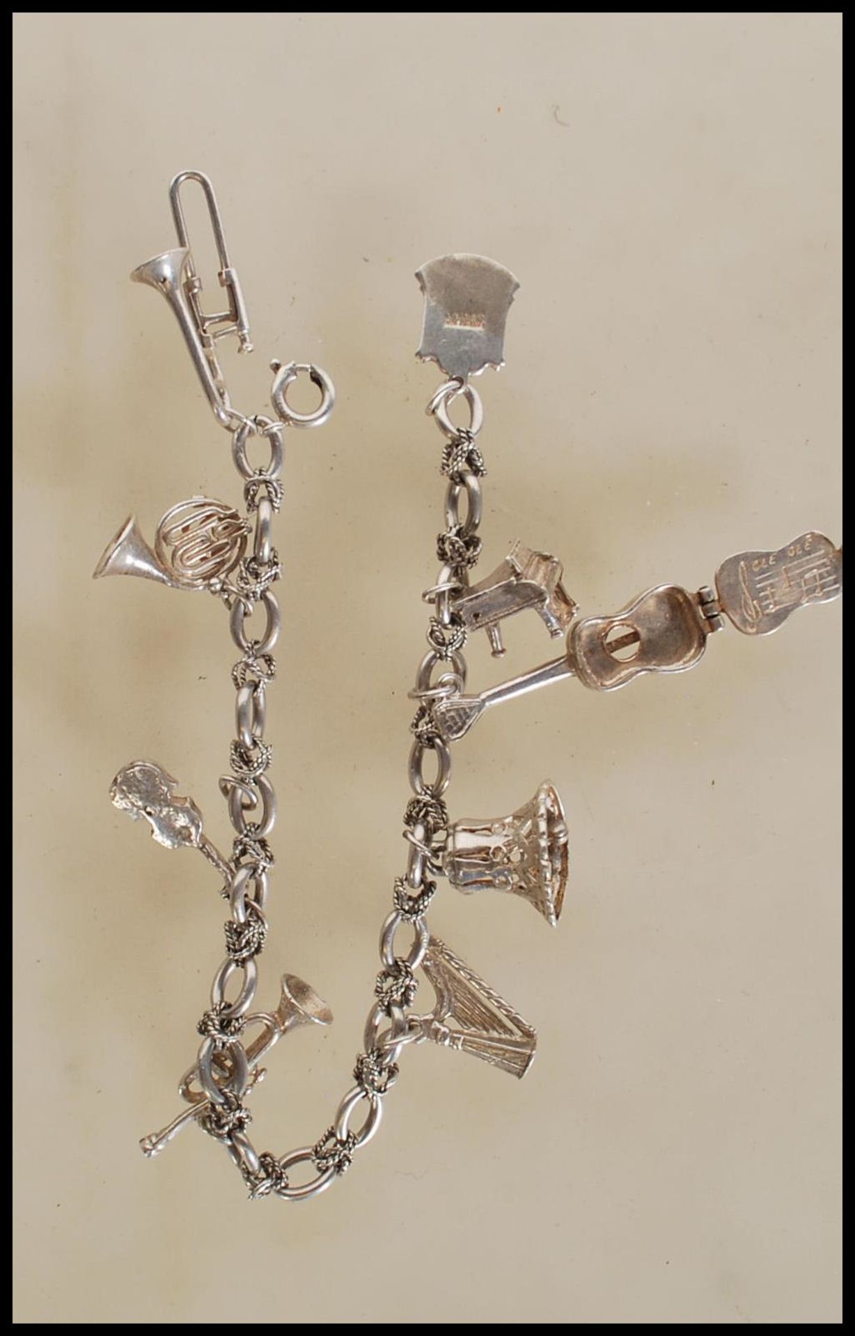 A silver charm bracelet having musical instrument charms to include trumpets, harp, bell violin,