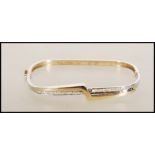 A hallmarked 9ct gold bangle of square form having a crossover of white and yellow gold, set with