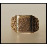 A hallmarked 9ct gold signet ring having a square unengraved head and bark effect shoulders.