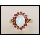 A stamped 9ct gold ring set with a central opal cabochon with a halo of red stones. Weight 4.7g.