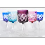 A set of six early 20th century multi coloured Bohemian glass wine glasses raised on faceted
