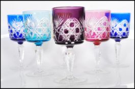 A set of six early 20th century multi coloured Bohemian glass wine glasses raised on faceted