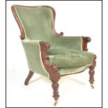 A Victorian mahogany library armchair being raised on turned legs with castors having green velour