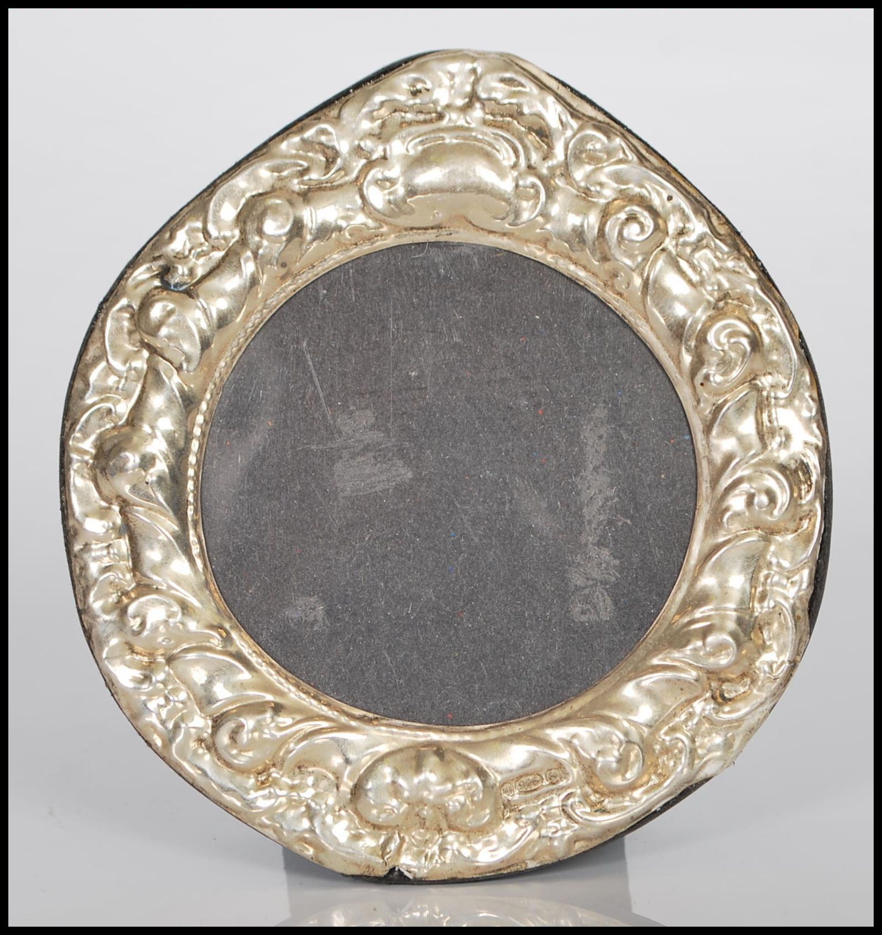 A sterling silver easel back photograph picture frame of circular form having rococo style relief
