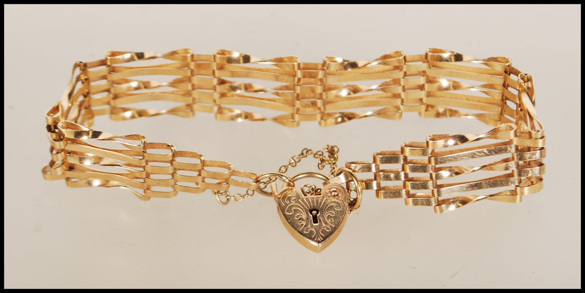 A hallmarked 9ct gold gate bracelet with tapered ends and attached heart-shaped padlock.