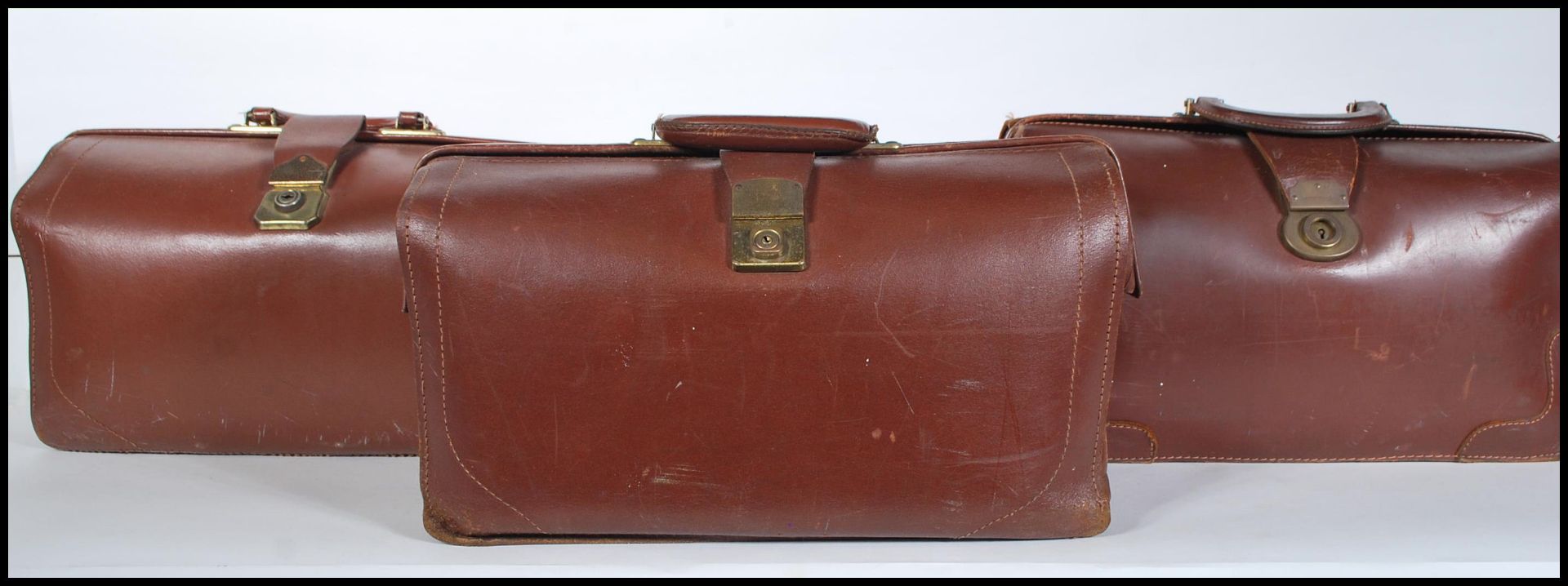 A collection of three vintage early to mid 20th Century Gladstone leather bags. Each having brass