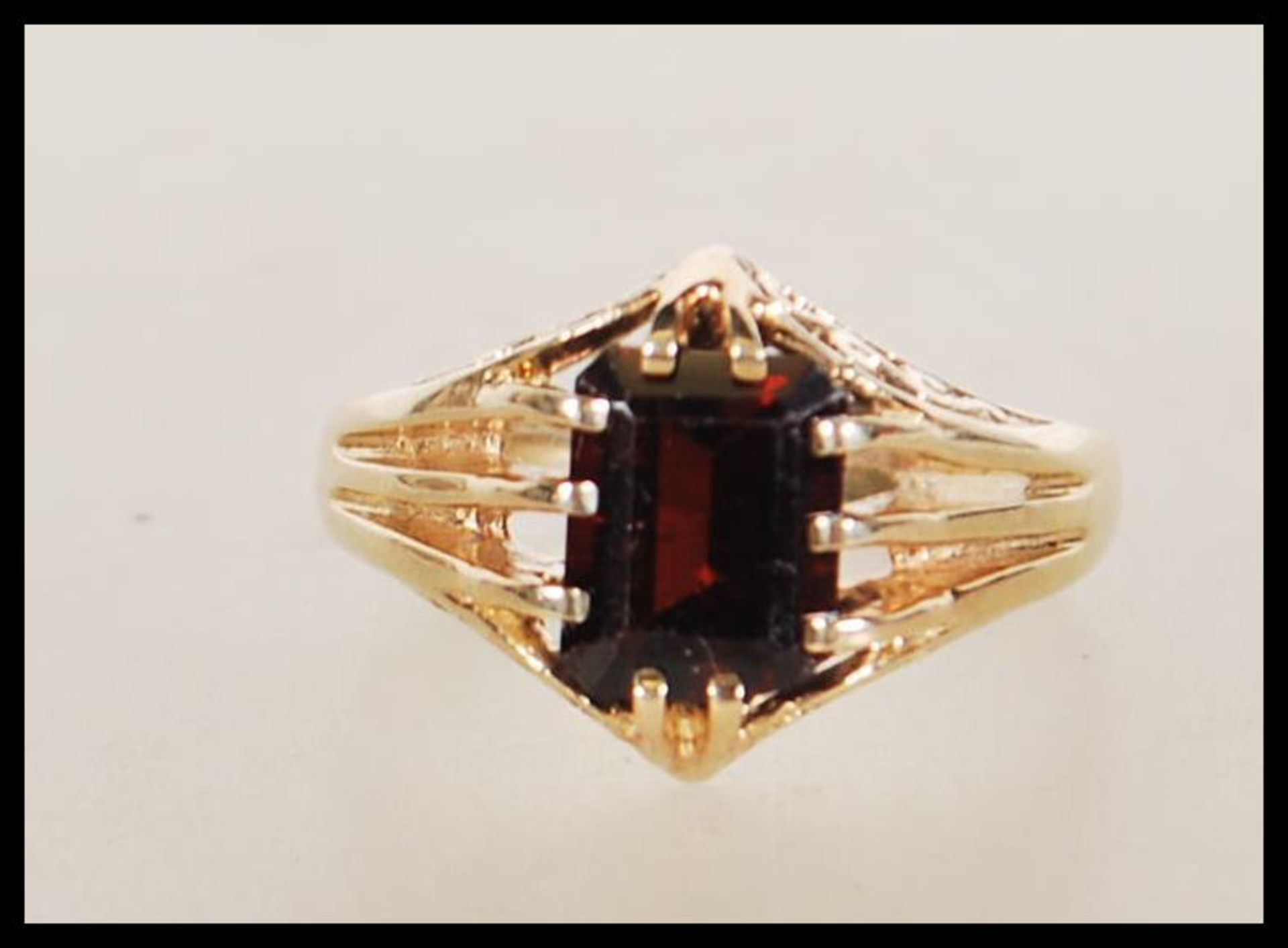 A hallmarked 9ct gold ring claw set with a rectangular cut red stone with reeded shoulders.