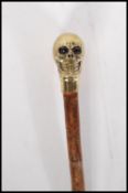 A contemporary walking stick cane having a brass knob handle in the form of skull on a bamboo shaft.