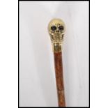 A contemporary walking stick cane having a brass knob handle in the form of skull on a bamboo shaft.