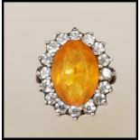 A stamped 9ct gold and silver ladies dress ring set with an oval cut orange stone with a halo of