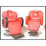 A pair of 20th Century red leatherette barbers chairs, scroll arms with adjustable headrests, raised