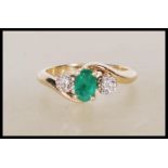 A hallmarked 9ct yellow gold ring having a prong set central emerald flanked by a cluster of