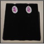 A pair of stamped 18ct white gold earrings having central faceted cut pink sapphires with a halo