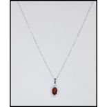 An 18ct white gold necklace pendant set with a central oval cut garnet with a halo of diamond accent