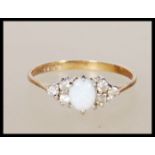 A hallmarked 9ct gold ring set with a opal cabochon flanked by six white accent stones. Hallmarked