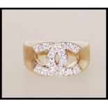 A stamped 9ct gold designer style ring with crossed C's to the head set with white accent stones.