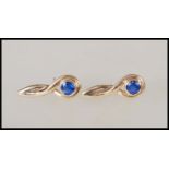 A pair of hallmarked 9ct gold earrings having a twist design set with two round cut sapphires.