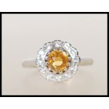 A hallmarked 9ct gold ring having central round cut orang stone surrounded by a halo of white stones