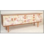 A mid 20th Century retro sideboard with a decoupage style front with fabric decorated cup handles.