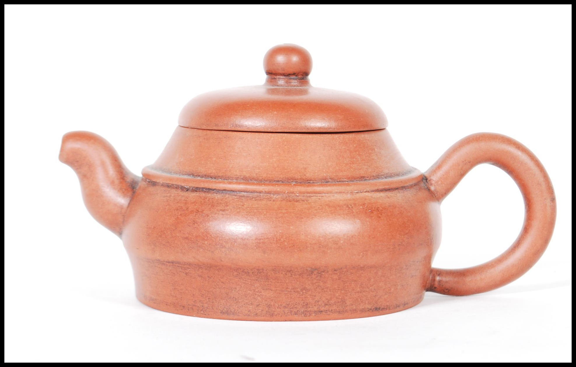 An early 20th Century Chinese Yixing teapot modelled in a brown clay with shaped handle and spout.