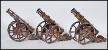 A set of three vintage 20th Century cast metal fireside cannons having a lustre finish, each set