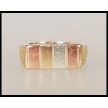 A hallmarked 9ct gold tri colour ring having a rectangular head with four shades of gold and bark