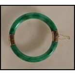 An oriental gold mounted green jade hinged bangle with two hinged sections of green jadeite united
