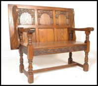A20th Century Old Charm oak monks bench, with a carved back and frieze, hinged seat, raised on stile