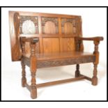 A20th Century Old Charm oak monks bench, with a carved back and frieze, hinged seat, raised on stile