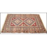 A vintage 20th Century Kazak hand knotted floor rug. Red ground, with stylised geometric borders and