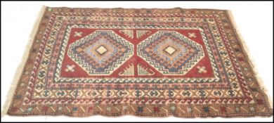 A vintage 20th Century Kazak hand knotted floor rug. Red ground, with stylised geometric borders and