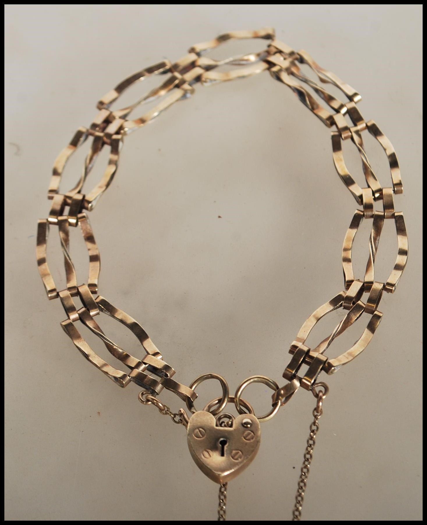 A 9ct gold hallmarked gate link bracelet having a heart padlock and safety chain. Hallmarked London.