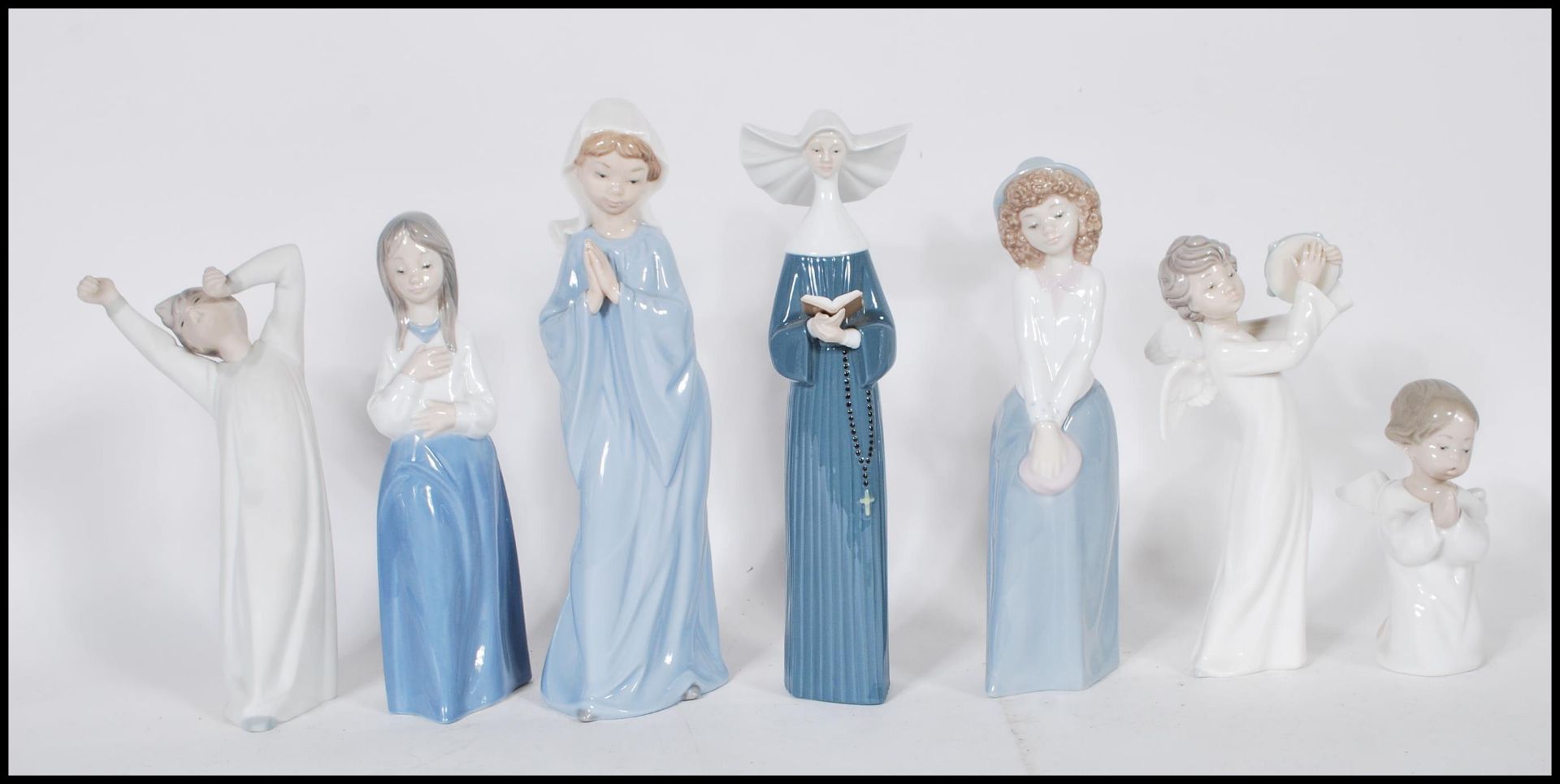 A collection of Nao and Lladro ceramic figurines to include a Lladro nun, a Lladro praying cherub,