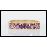 A hallmarked 9ct yellow gold ring set with five round cut purple stones with decorative scrolled