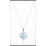 A silver drop pendant necklace set with a central faceted cut blue topaz having a halo of white