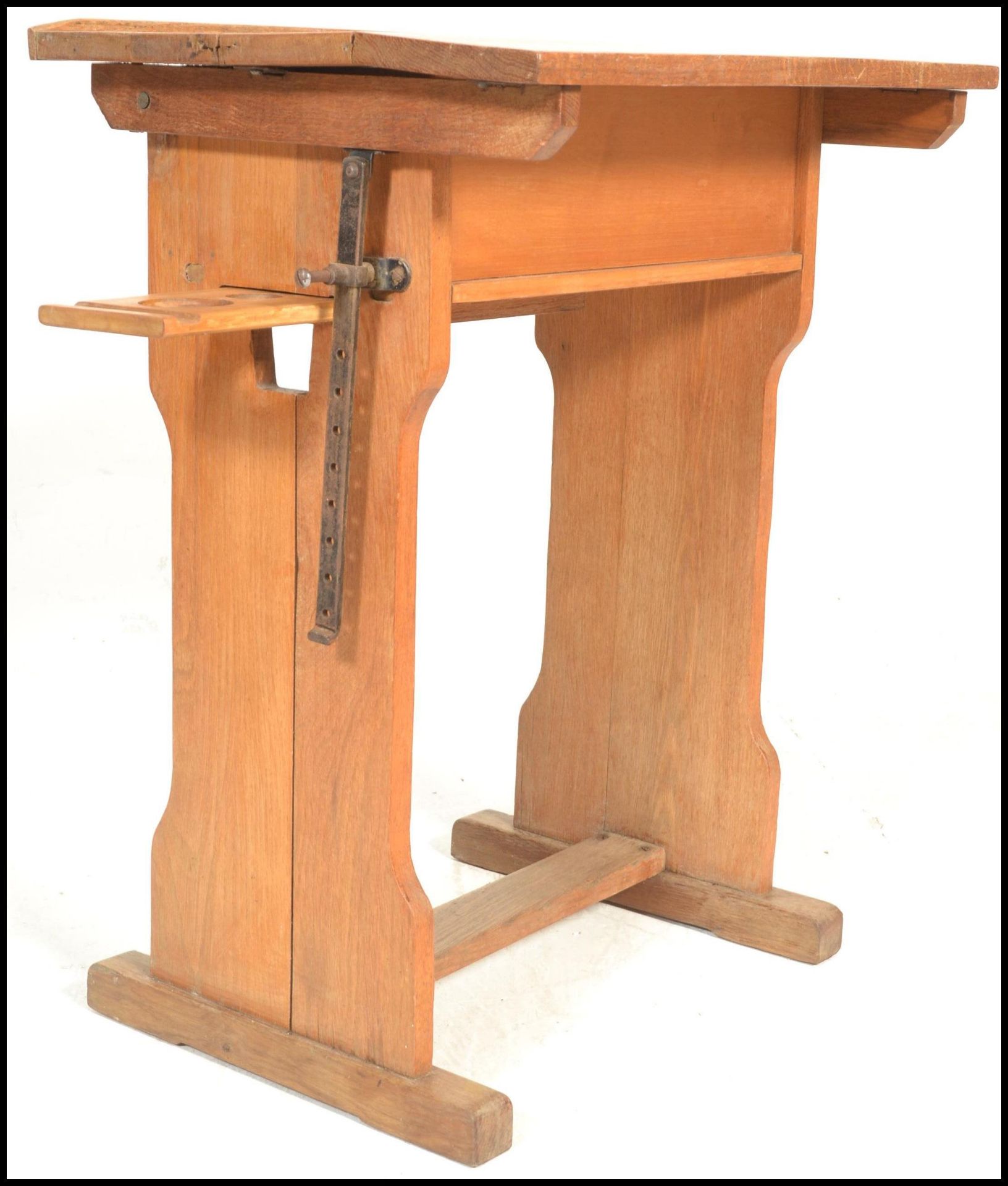 A vintage mid 20th Century beech school desk having adjustable tilt action to the top, swing out