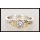 A 9ct two tone gold diamond solitaire ring having a bezel set brilliant cut diamond on a reeded