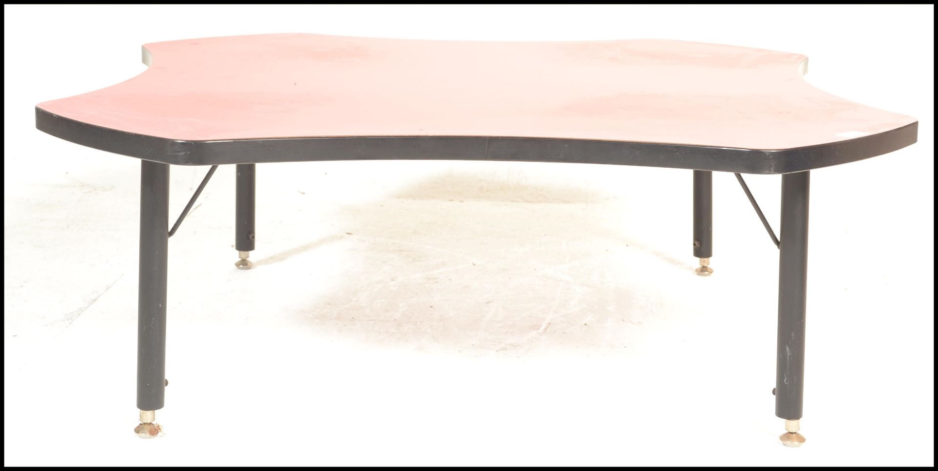 A 20th Century retro coffee table of square form having concave sides to the red top with ebonised