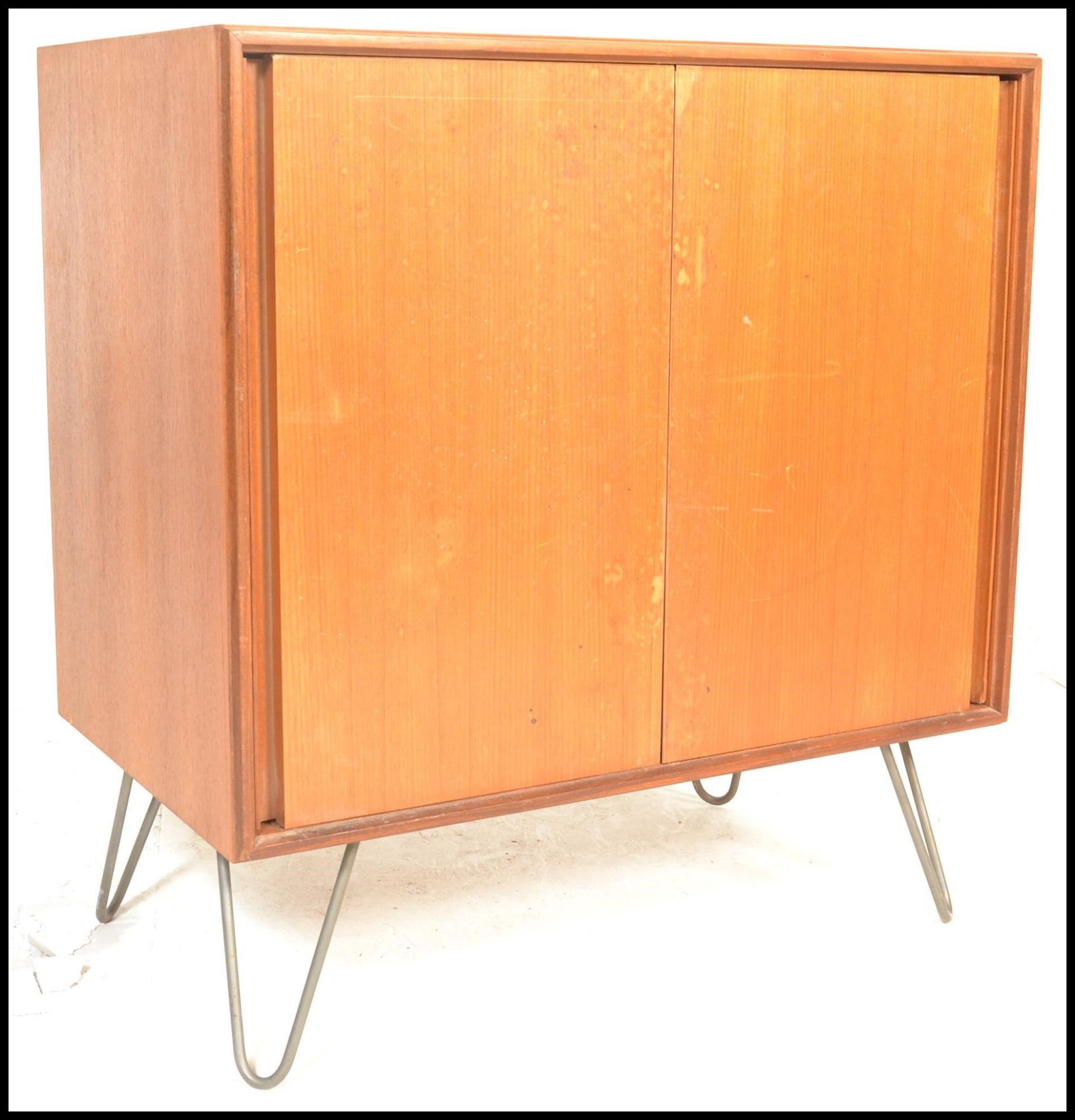 A mid century teak wood and hairpin leg cabinet. Raised on hairpin legs with a double door teak wood