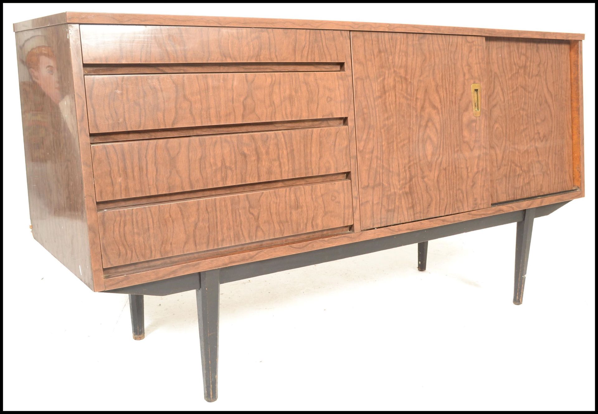 A mid century melamine sideboard credenza being raised on tapering legs with angled wide body