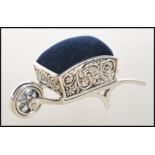 A stamped sterling silver pincushion in the from of wheelbarrow having embossed swirl and floral