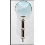 A contemporary large hand held magnifying glass of simple form having a silvered handled. Measures