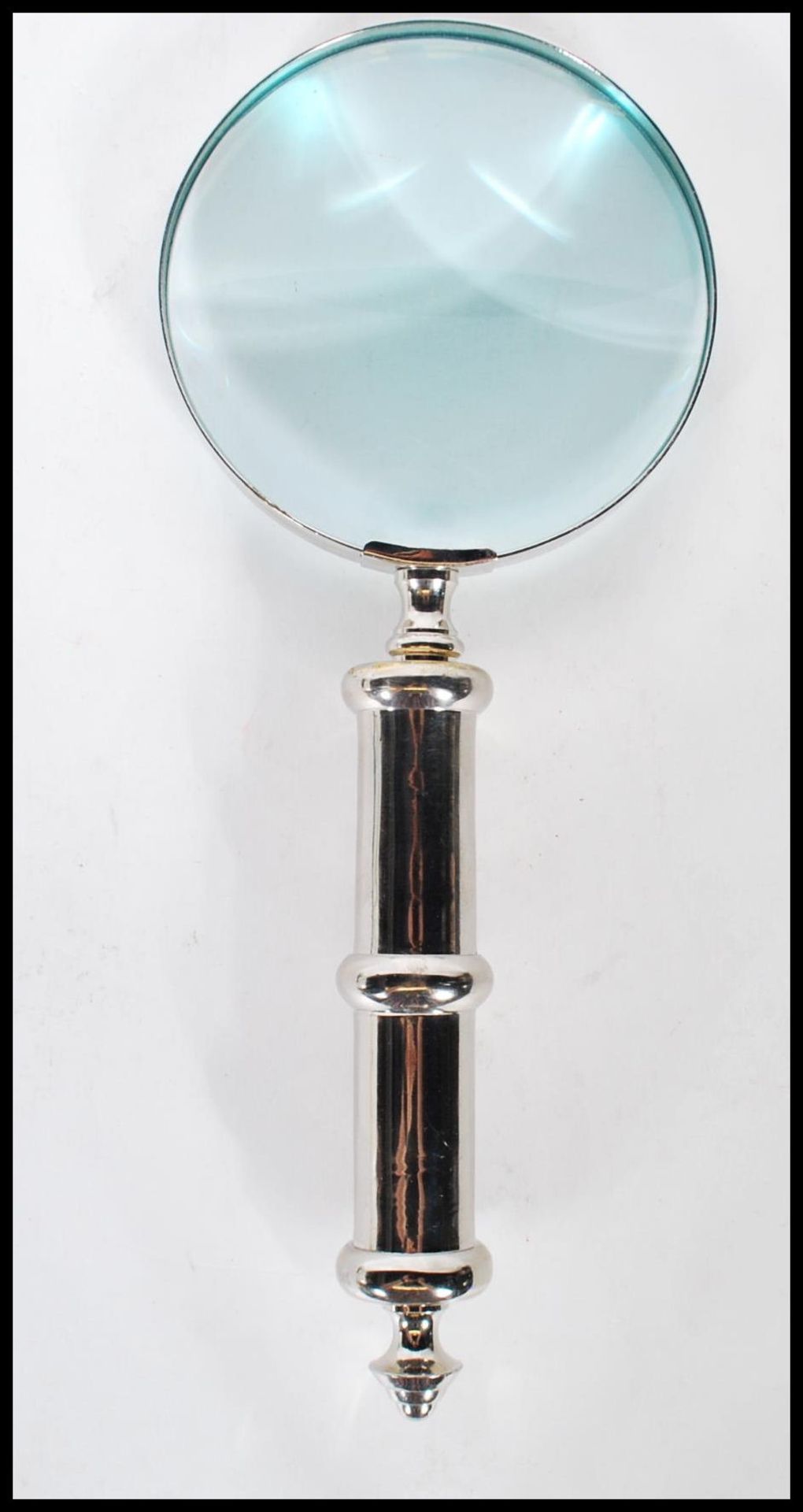 A contemporary large hand held magnifying glass of simple form having a silvered handled. Measures