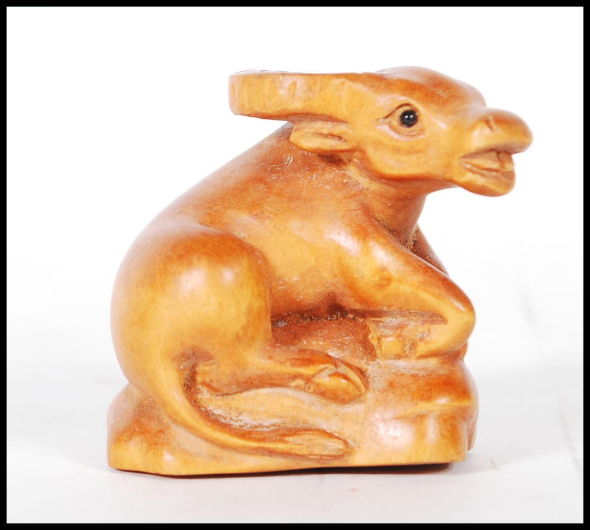 A detailed carved boxwood netsuke figure in the form of a laying yak. Measures 4cm tall by 4.5cm