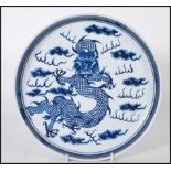 A 19th Century Chinese ceramic plate being hand painted in blue depicting a five toed dragon to