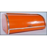 A retro 20th Century cylinder roll top wall mountable bread bin, original orange finish, printed