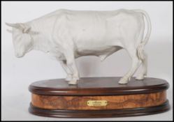 Alessandro Maggioni. A good Italian 1976 porcelain figurine of a bull raised on a walnut plinth with