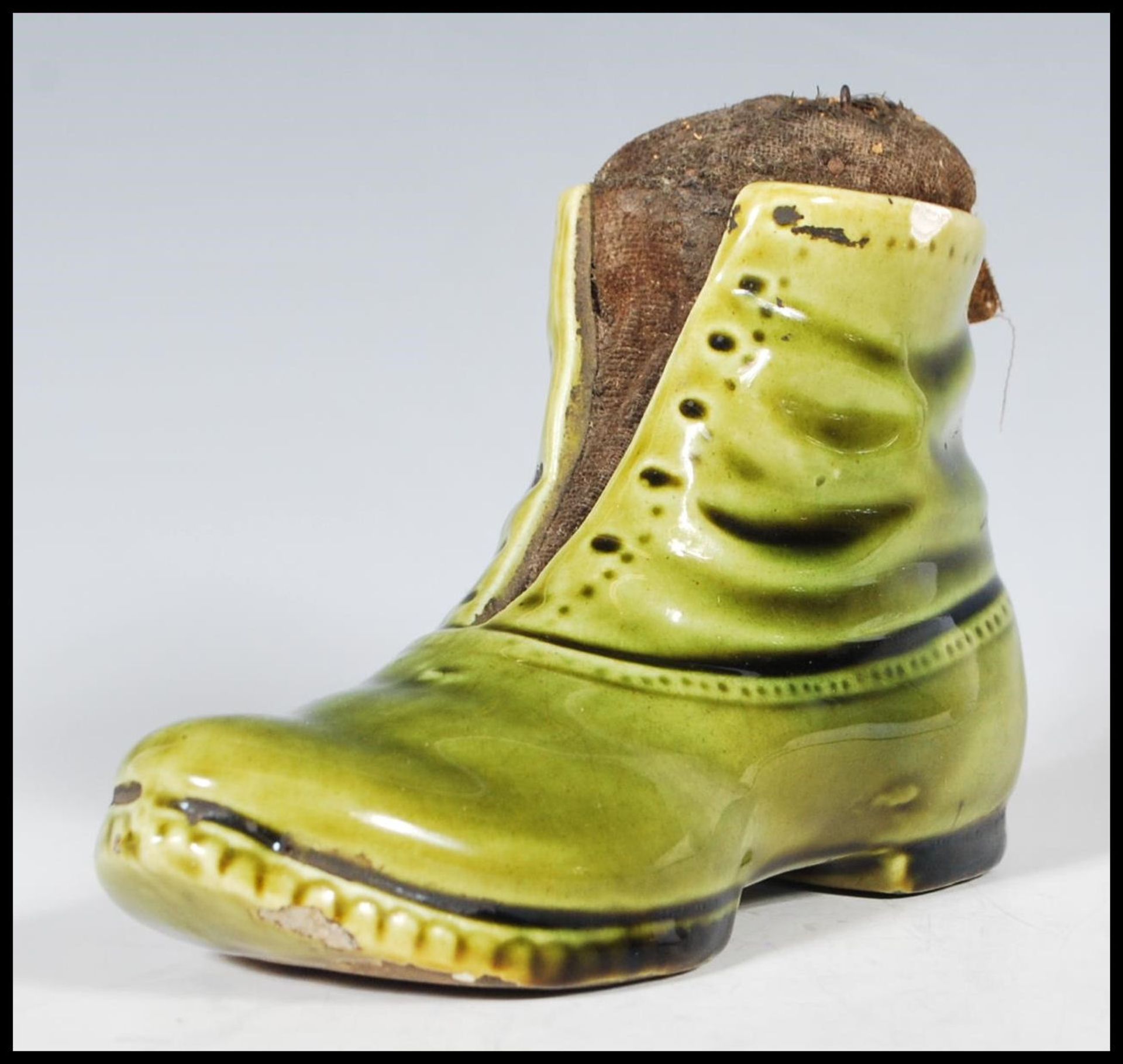 A 19th Century Victorian ceramic pin cushion in the form of boot having a green glaze with a straw