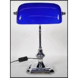 A vintage style bankers desk lamp having an adjustable blue glass shade raised on a chromed